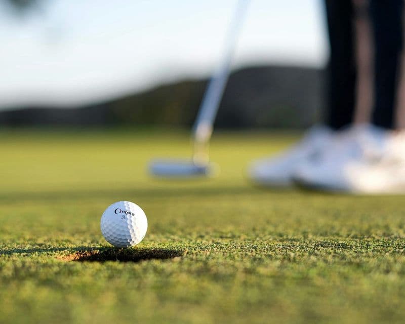 Golf ball at the edge of the hole with a putter behind