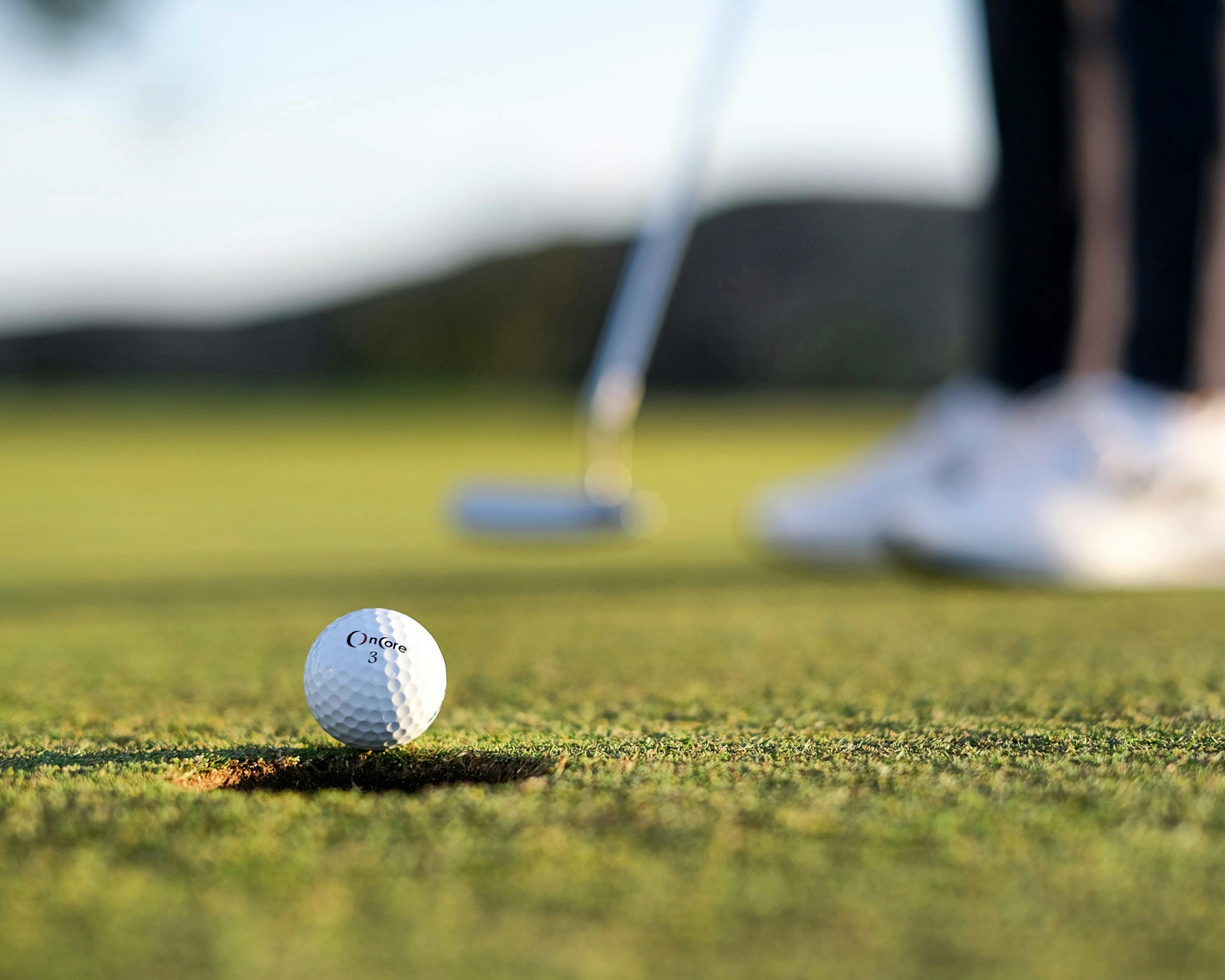 Golf ball at the edge of the hole with a putter behind