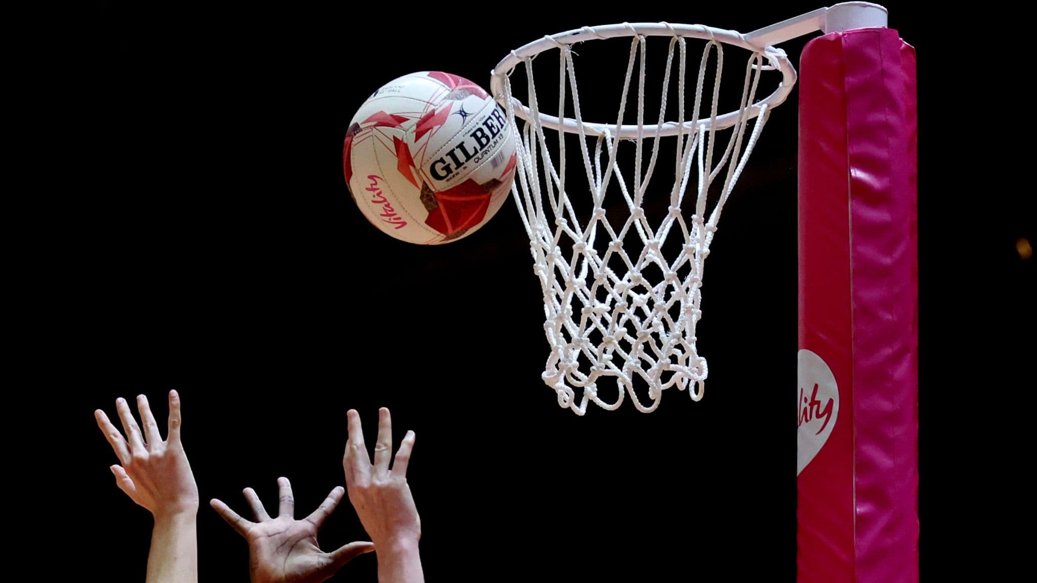 Netball going through the hoop with defender hands raised